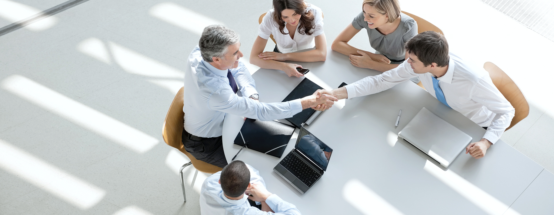 Overhead view of business partners shaking hands while sitting around conference table during board meeting.